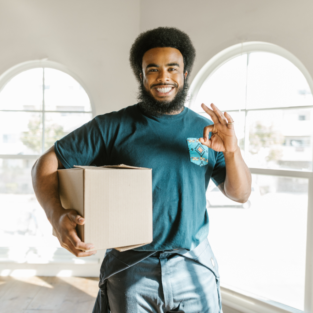 A smiling mover holding a small cardboard box and making an "OK" hand gesture after Moving in Edmonton with all boxes.